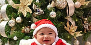 Roland Kyle is registered to the contest to win money with this photo: baby, child, christmas_tree, santa_claus_costume, holiday, festive, smiling, blanket, decoration, ornaments, ribbons, gold, red, indoor, cute, happy, seasonal, celebration, person, cozy