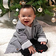 Roland Kyle joined the competition — help win amazing prizes! baby, child, smiling, coat, socks, christmas_tree, ornaments, ribbons, blanket, holiday, indoor, cute, festive, happy, celebration, person, infant, winter_clothing, decor, seasonal