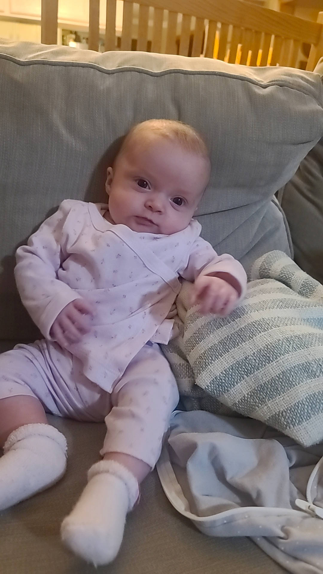 Isla is registered to the contest to win money with this photo: baby, baby_products, baby_toddler_clothing, cheek, chest, child, comfort, couch, foot, human_leg, knee, lap, leg, linens, person, sitting, sleeve, smile, sock, thigh