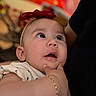 baby, blurred_background, bracelet, child, close_up, curious_expression, cute, face, headband, holding, indoor, infant, person, polka_dots, portrait, red_bow, skin, soft_background, white_clothing, wide_eyes