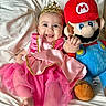 baby, bed, blanket, child, costume, crown, cute, happy, indoor, infant, mario, pink_dress, playful, plush_toy, portrait, princess, smile, soft, stuffed_animal, toy