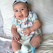 Aria is registered to the contest to win money with this photo: baby, blanket, bracelet, child, comfort, cushion, cute, dress, footwear, happy, headband, indoors, infant, person, portrait, sitting, small_hands, smiling, sock, soft_toys