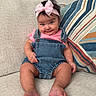 baby, child, infant, smile, denim_overalls, pink_bow, headband, couch, pillow, striped_pillow, sitting, indoor, cute, happy, portrait, person, skin, hand, foot, expression
