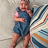 baby, child, smiling, denim_overalls, pink_headband, bow, couch, pillow, striped_pillow, happy, indoor, person, legs, feet, face, furniture, cute, sitting, infant, headwear