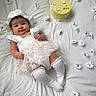 baby, infant, white_dress, daisy_pattern, hat, white_blanket, yellow_cake, flowers, daisies, celebration, milestone, cute, smiling, lying_down, portrait, soft_lighting, indoors, socks, happy, child