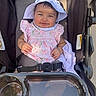 baby, child, smiling, stroller, hat, pink_clothing, floral_pattern, sunlight, happy, cute, infant, seatbelt, outdoor, person, portrait, baby_clothes, headwear, baby_girl, seat, daylight