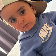 Nahil participe au concours pour gagner de l'argent avec cette photo : toddler, child, face, cap, hat, hoodie, blue_clothing, nike, indoor, portrait, curious, young_child, person, apparel, headwear, clothing, looking, casual, seated, expression