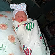 Hallie joined the competition — help win amazing prizes! newborn, baby, infant, sleeping, blanket, hat, bow, pillow, floral, indoors, cozy, cute, wrapped, resting, person, soft_light, nursery, decor, bedroom, peaceful