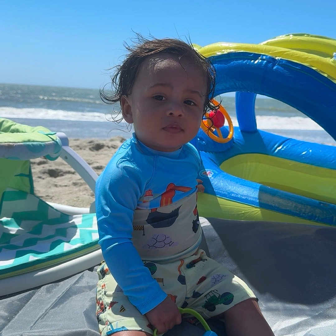 Slade joined the competition — help win amazing prizes! baby, beach, clothing, coast, face, head, lifejacket, nature, outdoors, person, photography, portrait, sea, shoreline, shorts, soil, summer, swimwear, vest, water