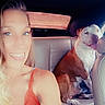 woman, dog, car_interior, selfie, smiling, seatbelt, tank_top, happy, pet, animal, leather_seat, tongue_out, casual, companion, daylight, portrait, transportation, friendship, blonde_hair, summer