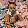 baby, child, infant, sitting, pacifier, hair_bows, smiling, face, portrait, bed, bedding, blanket, pillow, bedroom, indoor, toy, orange_toy, pink_bedding, patterned_fabric, crawling