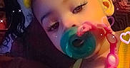 Calani is registered to the contest to win money with this photo: baby, child, infant, portrait, pacifier, yellow_bow, sleepy, face, eyes, long_eyelashes, smiling, yellow_clothing, bib, necklace, sitting, indoor, couch, adult_partial, sparkles, hearts