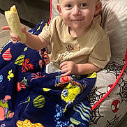 Matthias is registered to the contest to win money with this photo: toddler, child, banana, blanket, colorful, cushion, spiderman, cartoon, smile, indoor, happy, sitting, clothing, furniture, face, food, person, home, cute, cozy