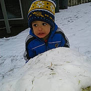 Alijah is registered to the contest to win money with this photo: child, snow, winter_clothing, hat, blue_jacket, outdoor, backyard, snow_mound, curious, cold_weather, grass, fence, window, trash_bins, person, play, season, daytime, young_child, expression