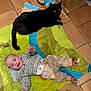baby, cat, black_cat, play_mat, floor, indoor, tiled_floor, child, infant, animal, pet, clothing, socks, toy, furniture, happy, lying_down, person, cute, cozy