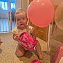 baby, child, balloons, gift, present, carpet, indoor, door, baby_gate, pink, wrapped_gift, floor, person, cute, celebration, party, infant, sitting, curious, home