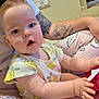 baby, child, infant, person, tattoo, clothing, sitting, indoor, holding, curious, cute, yellow, pattern, skin, face, arm, lap, pink, relaxed, home