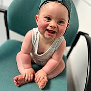 Charles participe au concours pour gagner de l'argent avec cette photo : baby, child, smiling, cap, green_cap, chair, sitting, cross_legged, indoor, person, cute, happy, face, skin, infant, clothing, headwear, seat, young_child, toddler