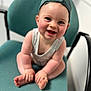 baby, child, smiling, cap, green_cap, chair, sitting, cross_legged, indoor, person, cute, happy, face, skin, infant, clothing, headwear, seat, young_child, toddler