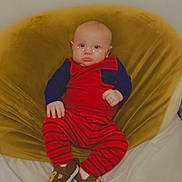 Asher is registered to the contest to win money with this photo: baby, child, infant, red_clothing, striped_pants, monkey_slippers, yellow_chair, velvet_chair, indoor, person, cute, sitting, face, feet, footwear, digital_effects, star_overlay, relaxed, home, soft_furniture