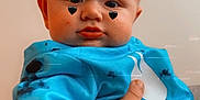 Asher is registered to the contest to win money with this photo: baby, blue_shirt, child, closeup, clothing, cute, expression, eyes, face, hand, heart_filter, holding, indoor, person, portrait, skin, smile, tattoo, tie_dye, young_child