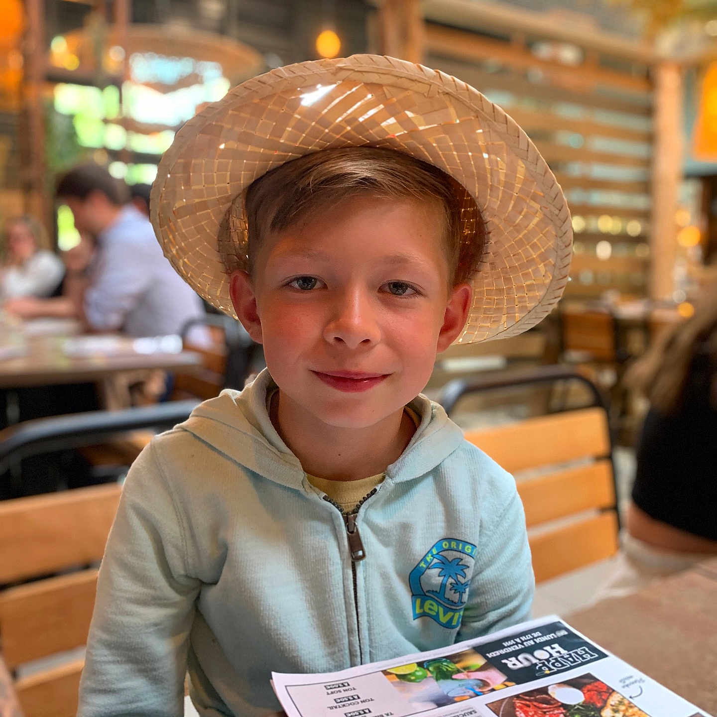 Tiago a rejoint le concours — aidez-le/la à gagner de superbes lots ! blurry_background, boy, casual_clothing, child, face, hat, hoodie, indoor, levis, light, menu, person, portrait, restaurant, seated, smile, straw_hat, table, wooden_chair, young