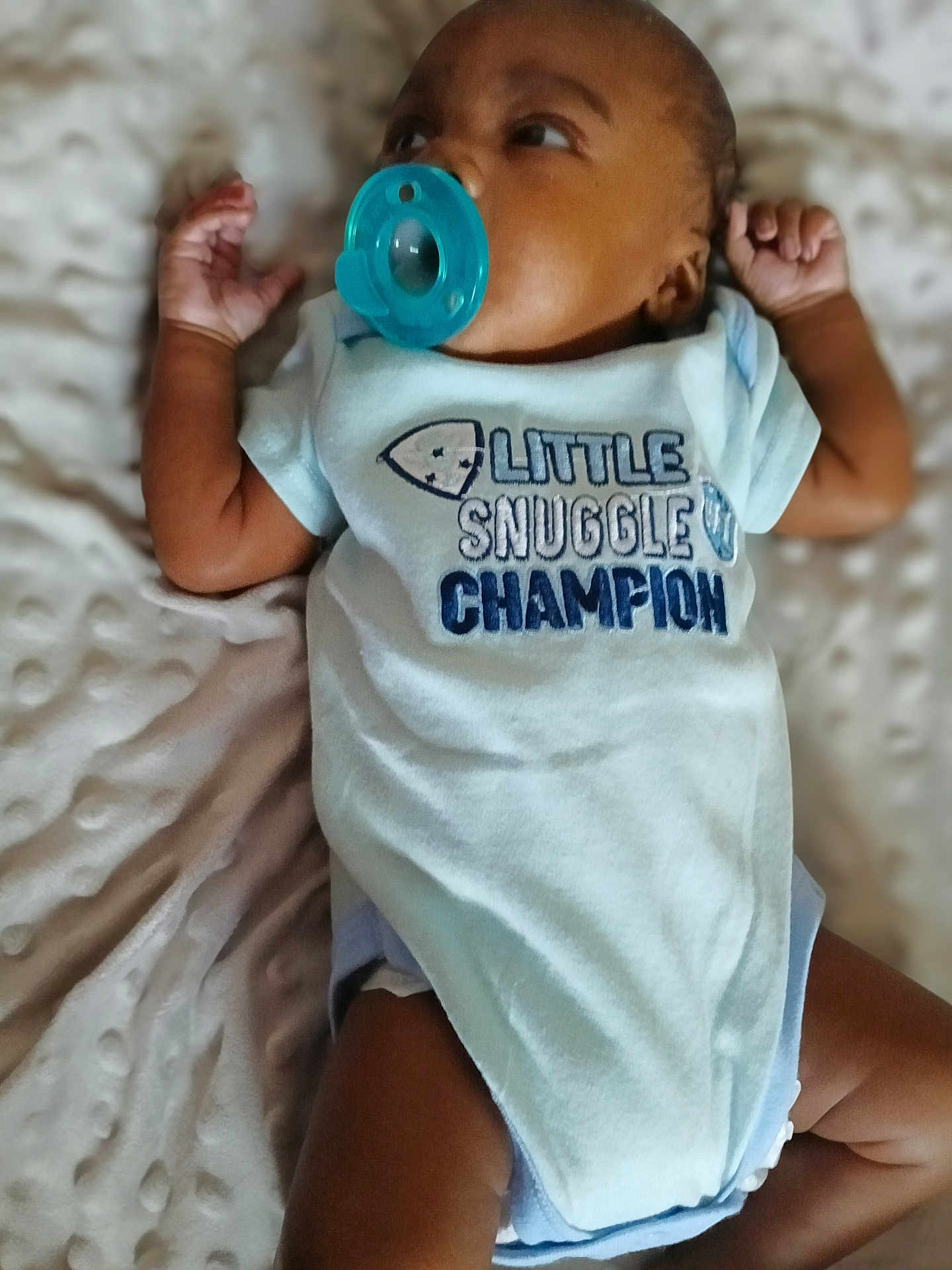 K'Rson is registered to the contest to win money with this photo: baby, infant, pacifier, onesie, clothing, lying_down, blanket, soft_texture, cute, child, newborn, skin, hand, face, head, sleepwear, indoors, comfortable, toddler, snuggle