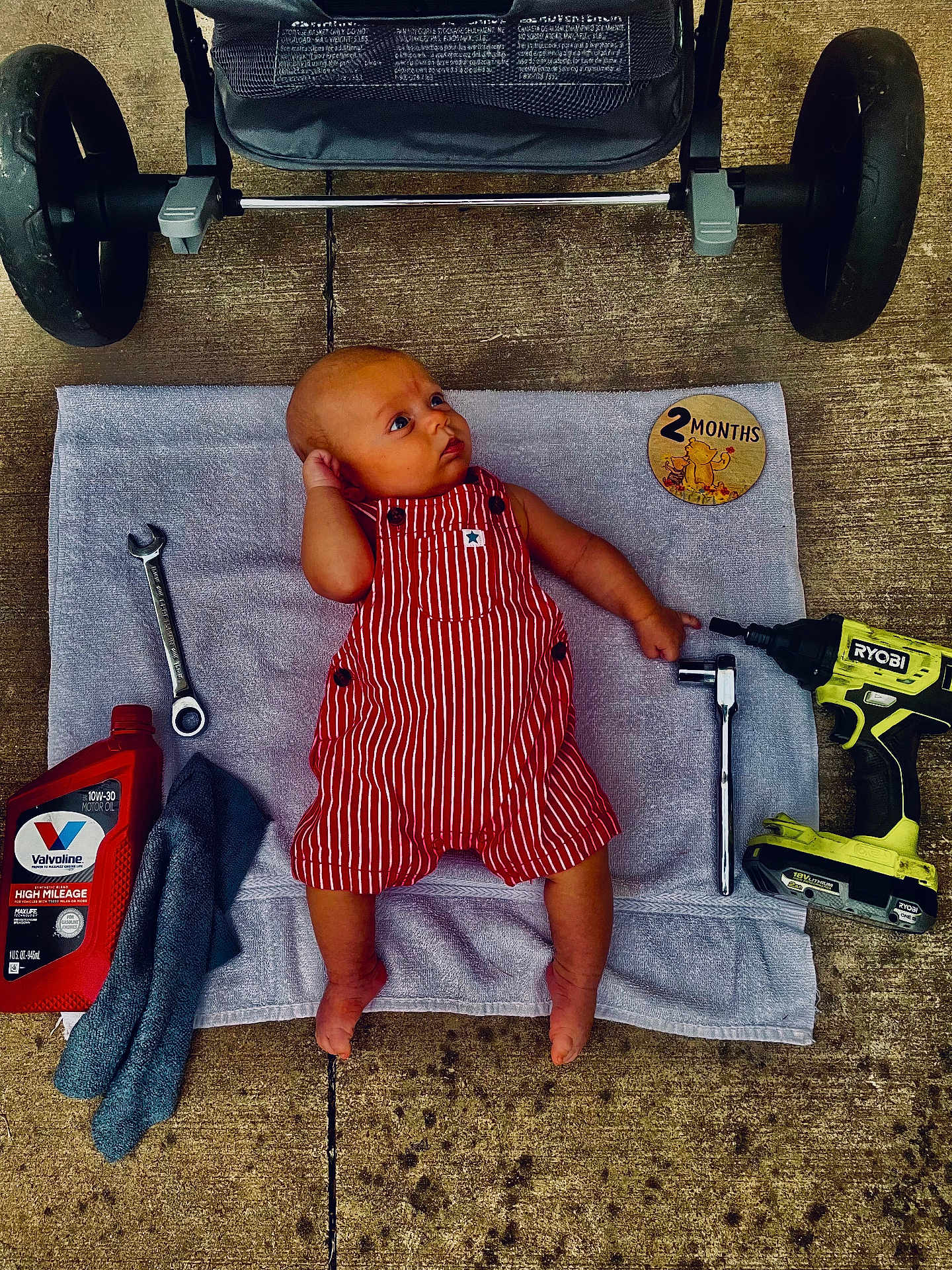 Trenton joined the competition — help win amazing prizes! baby, baby_pose, barefoot, child, clothing, concrete, cute, drill, floor, infant, mechanic, oil_bottle, outdoor, red, striped, toddler, tools, towel, workshop, wrench