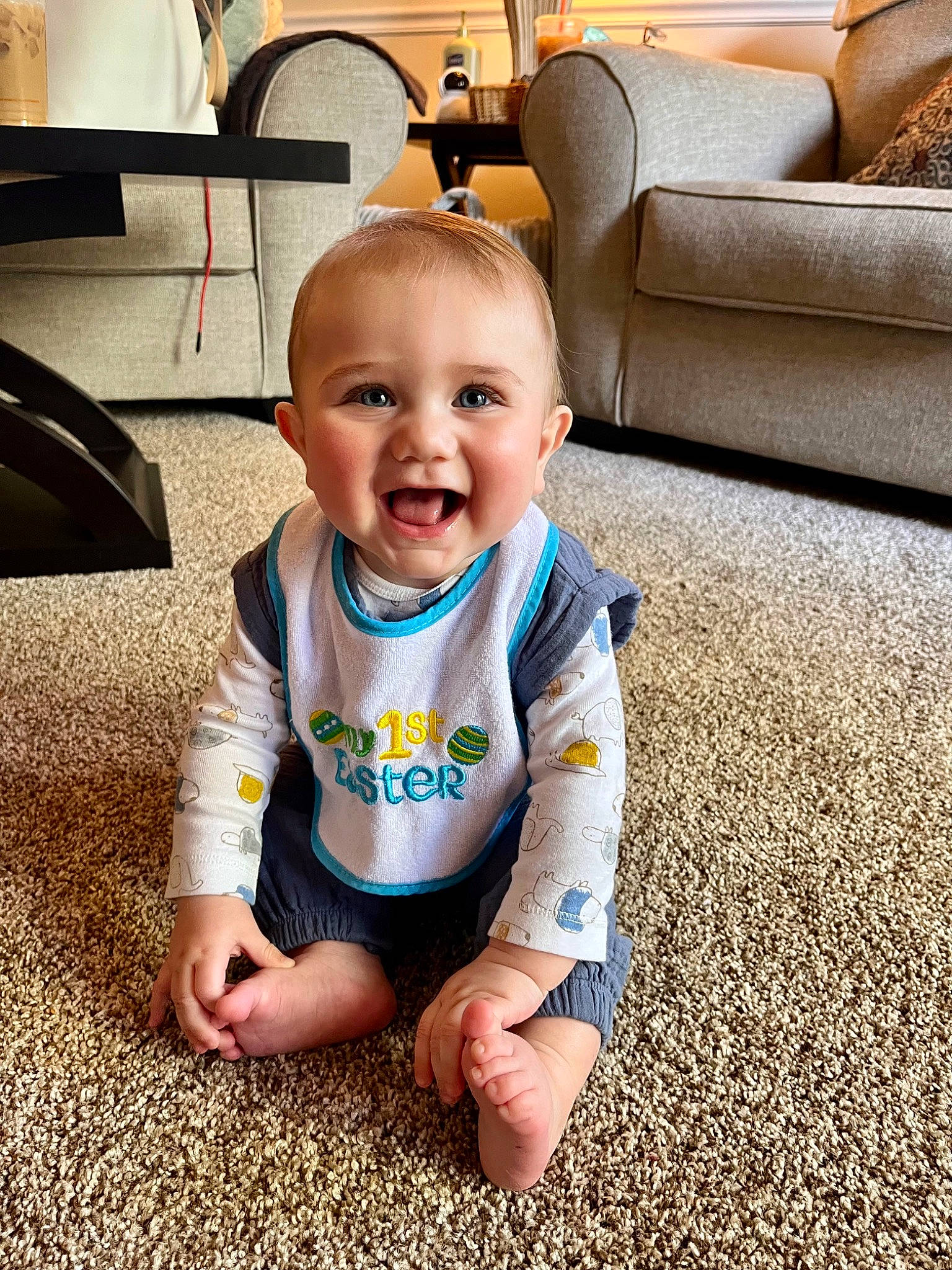 Brooks is registered to the contest to win money with this photo: baby, baby_toddler_clothing, cheek, comfort, eye, facial_expression, finger, floor, flooring, furniture, happy, head, joy, leg, person, skin, sleeve, smile, standing, t_shirt