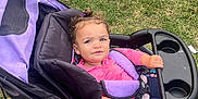 Cienna is registered to the contest to win money with this photo: toddler, stroller, grass, outdoor, child, playground, jacket, jeans, footwear, purple, black, pink, seatbelt, wheel, hand, face, person, nature, daylight, park