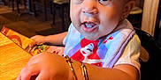 Aubree joined the competition — help win amazing prizes! toddler, child, curly_hair, pink_bow, bracelets, bib, restaurant, wooden_table, menu, indoor, portrait, cute, happy, seated, person, closeup, bright_lighting, expression, curious, casual_clothing