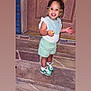 beads, braided_hair, child, cute, door, doorstep, footwear, green, happy, outdoor, person, portrait, shorts, smiling, snack, sneakers, standing, stone, toddler, white_top