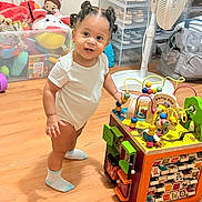 Aubree is registered to the contest to win money with this photo: toddler, child, toy, bead_maze, wooden_floor, indoor, play, curious, smiling, socks, furniture, storage_boxes, toys, person, cute, hair_buns, colorful, learning_toy, floor, playroom