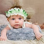 baby, infant, flower_crown, blue_eyes, soft_texture, cushion, blanket, indoor, portrait, cute, child, headband, closeup, resting, skin, small_hands, lying_down, soft_lighting, cozy, adorable