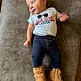 baby, child, infant, tshirt, boots, pants, smile, face, hand, footwear, clothing, lying_down, curious, indoor, soft_surface, light_skin, short_hair, casual_wear, portrait, cute