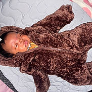 Icelynn is registered to the contest to win money with this photo: baby, sleeping, fur_suit, brown, quilt, toy, infant, child, cute, cozy, hood, zipper, soft, indoors, rest, peaceful, face, head, blanket, person