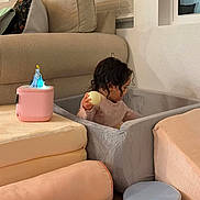 Sarah a rejoint le concours — aidez-le/la à gagner de superbes lots ! toddler, child, playpen, cushions, toy, ball, speaker, figurine, cinderella, living_room, sofa, window, blinds, floor, curly_hair, indoor, soft_toys, pastel_colors, cozy, relaxing