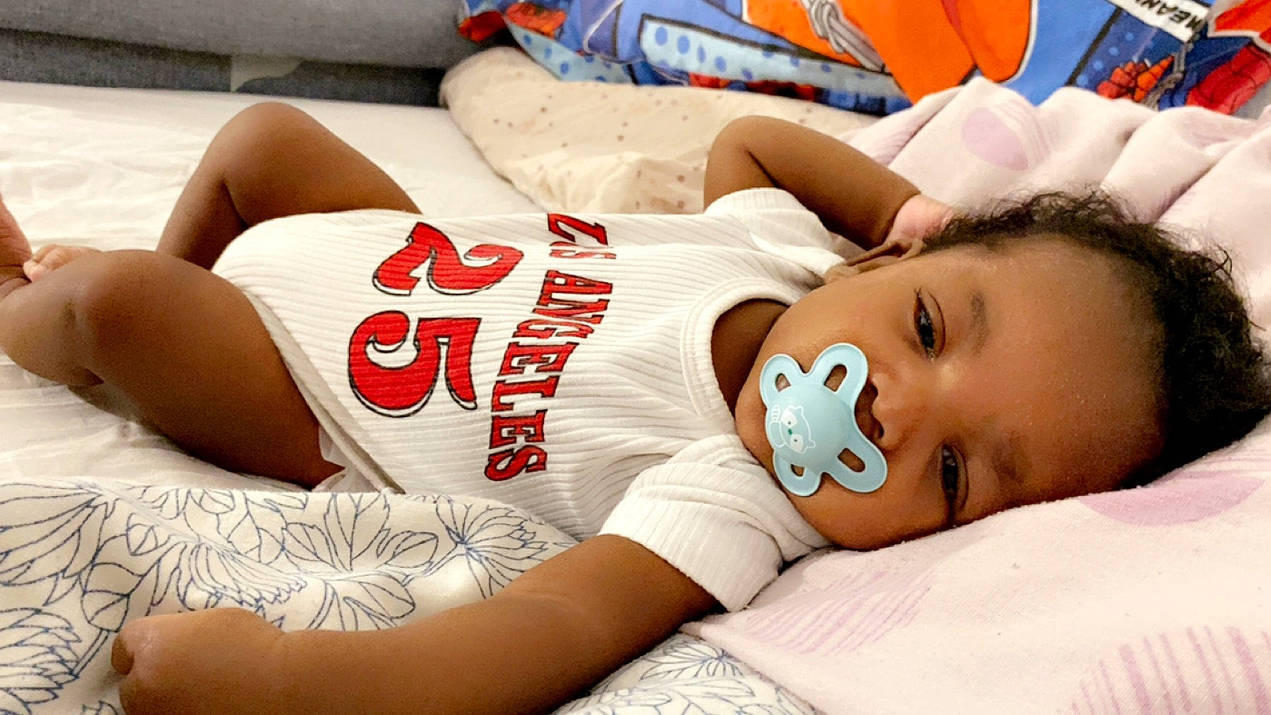 Issa participe au concours pour gagner de l'argent avec cette photo : abdomen, bedding, carmine, chest, child, comfort, elbow, flesh, happy, human_leg, jersey, knee, linens, person, room, sitting, sleeveless_shirt, sportswear, t_shirt, thigh