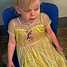 Amirah is registered to the contest to win money with this photo: child, dress, yellow, princess, blue_chair, headband, ears, blonde_hair, indoor, floor, wall, person, sitting, costume, portrait, young_child, looking_away, fabric, cute, casual