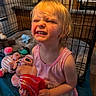 child, playpen, toy, doll, stuffed_animal, indoor, pink_clothing, blonde_hair, expression, face, person, play, cute, smile, baby, cage, floor, bed, room, happy