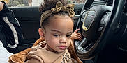 Nevaeh joined the competition — help win amazing prizes! car, casual_clothing, child, cloudy_sky, curious, curly_hair, hand, headband, interior, jacket, lap, outdoor, person, portrait, seat, sitting, steering_wheel, toddler, trees, window