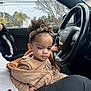 car, casual_clothing, child, cloudy_sky, curious, curly_hair, hand, headband, interior, jacket, lap, outdoor, person, portrait, seat, sitting, steering_wheel, toddler, trees, window