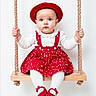baby, child, swing, red_hat, red_dress, white_tights, red_shoes, rope, wooden_swing, blue_eyes, indoor, portrait, cute, childrens_fashion, sitting, holding, studio, white_background, expression, innocence
