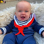 Jaxson is registered to the contest to win money with this photo: baby, child, smiling, outdoor, blue_clothing, red_scarf, striped_shirt, fluffy_cushion, happy, face, head, sitting, person, infant, playful, garden, brick_wall, toy, footwear, casual