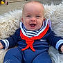 baby, child, smiling, outdoor, blue_clothing, red_scarf, striped_shirt, fluffy_cushion, happy, face, head, sitting, person, infant, playful, garden, brick_wall, toy, footwear, casual
