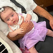 Sariah joined the competition — help win amazing prizes! baby, infant, adult, holding, purple_skirt, fuzzy_socks, white_shirt, black_tie, tattoo, indoor, seated, curious_expression, hand, arm, person, clothing, fabric, closeup, portrait, cute