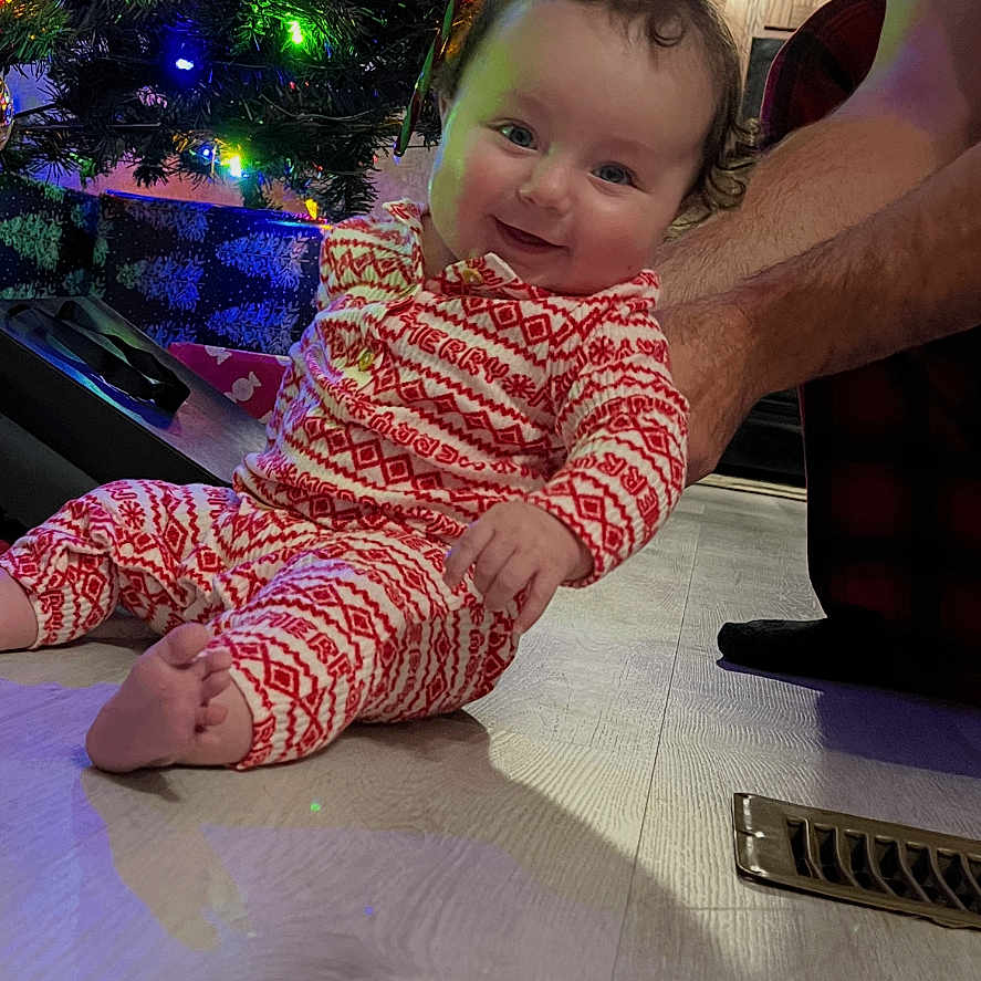 Sariah joined the competition — help win amazing prizes! adult_arm, baby, celebration, child, christmas_tree, cozy, decorations, festive, floor, happy, holiday, home, indoor, lights, ornaments, pajamas, person, seasonal, smiling, wood_floor