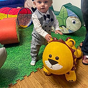 Jensen is registered to the contest to win money with this photo: toddler, child, toy, lion_toy, playroom, play_mat, colorful, vest, bow_tie, indoor, flooring, person, feet, hand, cushion, tunnel_toy, smile, blond_hair, cute, standing