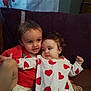 child, baby, couch, pillow, heart_pattern, red_clothing, white_clothing, diaper, indoor, cute, siblings, family, portrait, smiling, curious, toddler, cuddling, plush, relaxed, home
