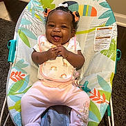 Skylar is registered to the contest to win money with this photo: baby, baby_rocker, bib, carpet, child, clothing, colorful, cute, floor, hair_bows, happy, indoor, infant, pacifier, person, pink_pants, seat, smiling, toy, wall